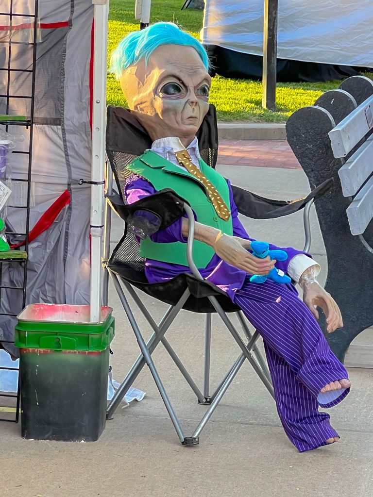 An alien passing the time with some people watching on the street