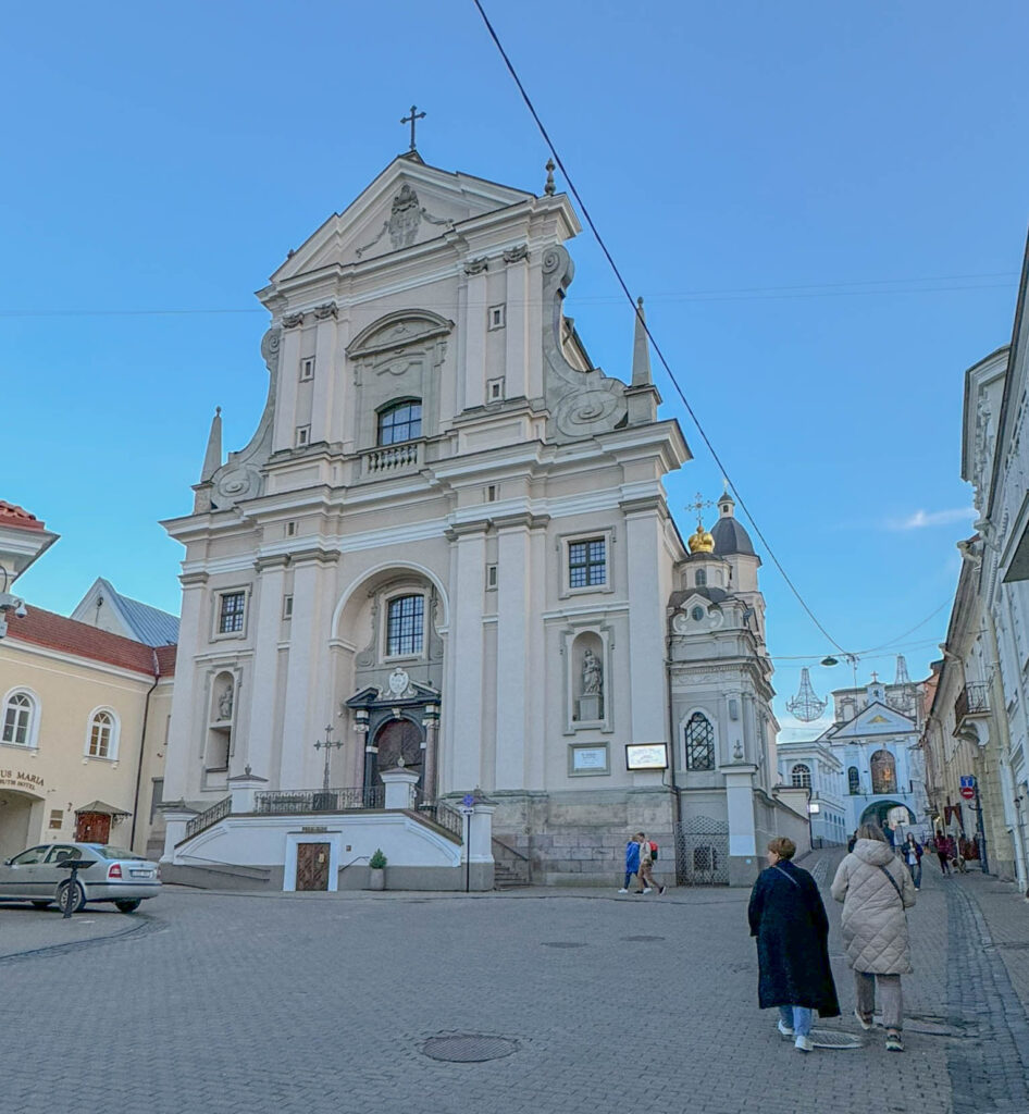 A photo of the Church of St. Theresa (Šv. Teresės bažnyčia) in Vilnius Old Town, located near the Gate of Dawn. Built in the Baroque style in the early 17th century, it is one of the city's most prominent religious landmarks. The church is known for its richly decorated interior, featuring ornate altars and frescoes. It's closely associated with the Carmelite Order and is part of a significant spiritual route leading to the Gate of Dawn Chapel, which houses the revered icon of Our Lady of the Gate of Dawn.