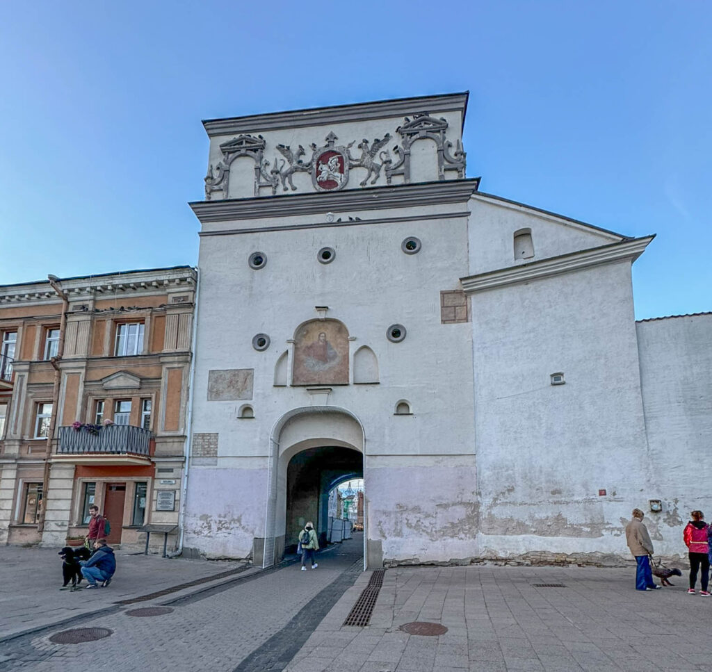 This is the Gate of Dawn (Aušros Vartai) as seen from the outer side of the city, facing away from the inner Old Town of Vilnius. The gate was originally part of the city's defensive walls, built in the early 16th century. The structure is adorned with Lithuania's coat of arms, the Vytis (a knight on horseback), and features an exterior niche with a religious painting, emphasizing its dual role as both a defensive and religious monument. The Gate of Dawn Chapel, located on the inner side of the gate, houses the famous icon of Our Lady of the Gate of Dawn, which draws pilgrims from across the region. This view highlights the historical and architectural significance of the gate as a symbol of Vilnius' heritage and resilience.