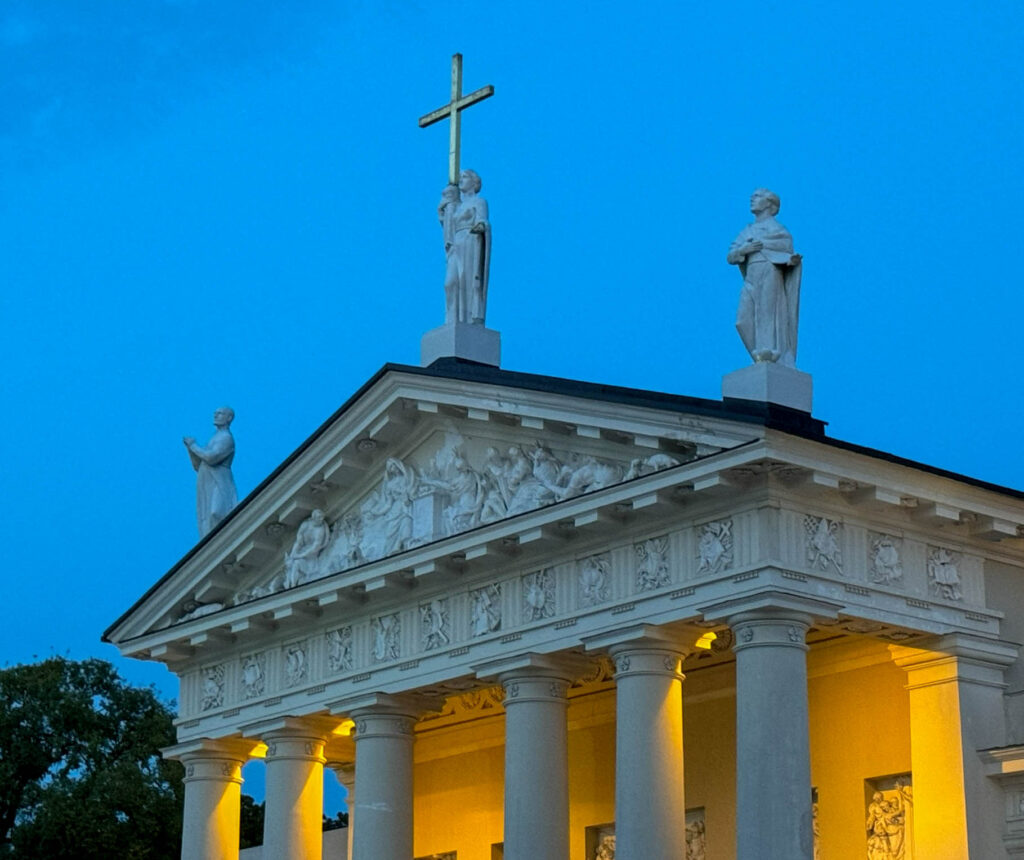 The statues on top of the Vilnius Cathedral in the photo are representations of three significant Christian figures: Saint Casimir (left side) - the patron saint of Lithuania, known for his piety and dedication to helping the poor; Saint Helena (center, holding the cross) - the mother of Emperor Constantine the Great, credited with discovering the True Cross of Christ; and Saint Stanislaus (right side) - the patron saint of Poland and one of the most important figures in the religious history of the region.