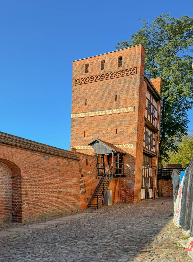 The Leaning Tower of Toruń, known locally as Krzywa Wieża, is one of the most iconic medieval landmarks in the city. Built in the 13th century as part of the defensive walls, the tower now leans about 5 feet (1.5 meters) due to unstable ground beneath it. Its unusual tilt draws plenty of visitors. Local legend says that a Teutonic Knight broke his vows by falling in love with a local woman. As punishment for his betrayal, he was ordered to construct a crooked tower to reflect his “crooked” actions. Today, it’s a popular spot where tourists test their balance by standing with their back and heels against the slanted wall, arms outstretched. If they remain steady, they’re considered “innocent.” If they wobble, well, the tower has its judgment.