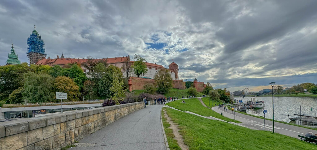 Wawel Castle, one of Kraków's most famous landmarks, sits proudly on Wawel Hill, overlooking the Vistula River. Once a royal residence, the castle stands as a testament to Poland's rich history and culture, showcasing a blend of Romanesque, Gothic, Renaissance, and Baroque architectural styles. Below, the peaceful Vistula River Boulevards offer a favorite spot for walking and cycling, with stunning views of the castle, the historic city, and modern touches like a distant Ferris wheel.