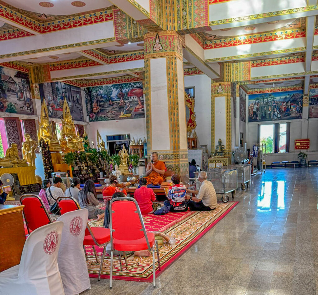 A small group gathers around a monk inside Wat Nong Wang, taking part in what looks like a blessing or teaching.